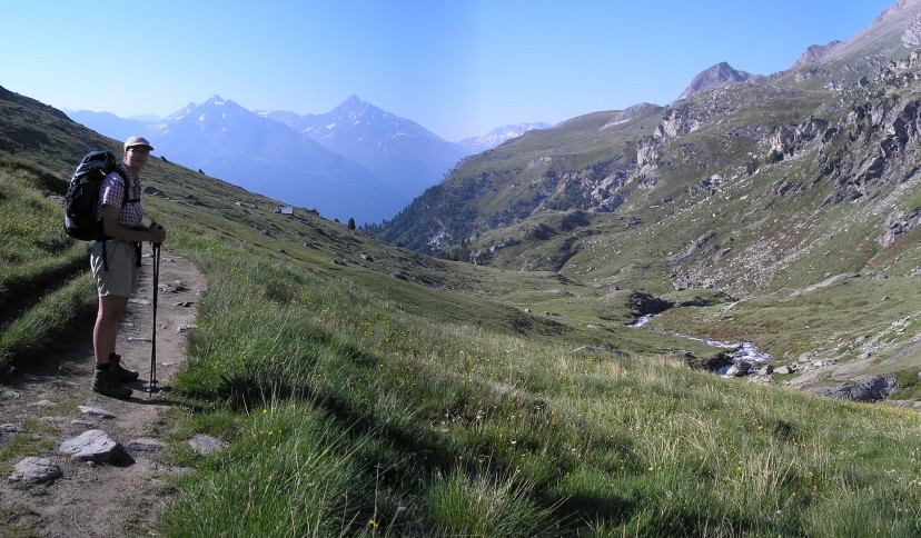 Djuke stands on a path at the side of a grassy apline valley